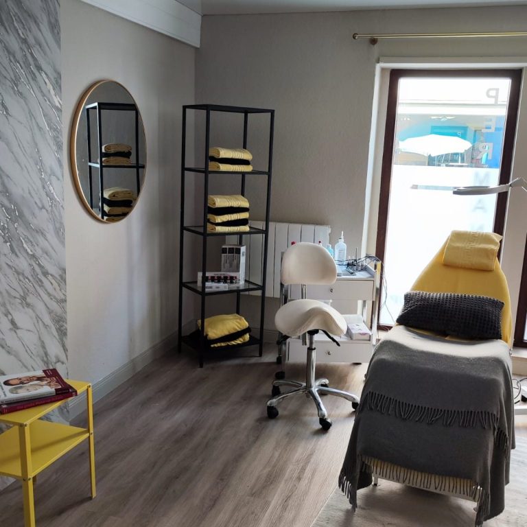 Kosmetikstudio Helles Behandlungszimmer mit einem Behandlungsstuhl, Regal und rundem Spiegel.