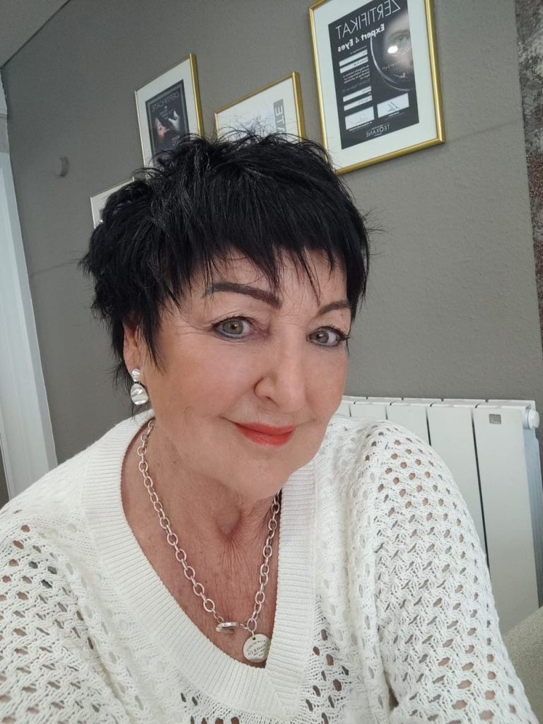 Feodora Pradt Porträt einer Frau mit kurzen dunklen Haaren, hellen Lippen und Schmuck, in einem hellen Raum.