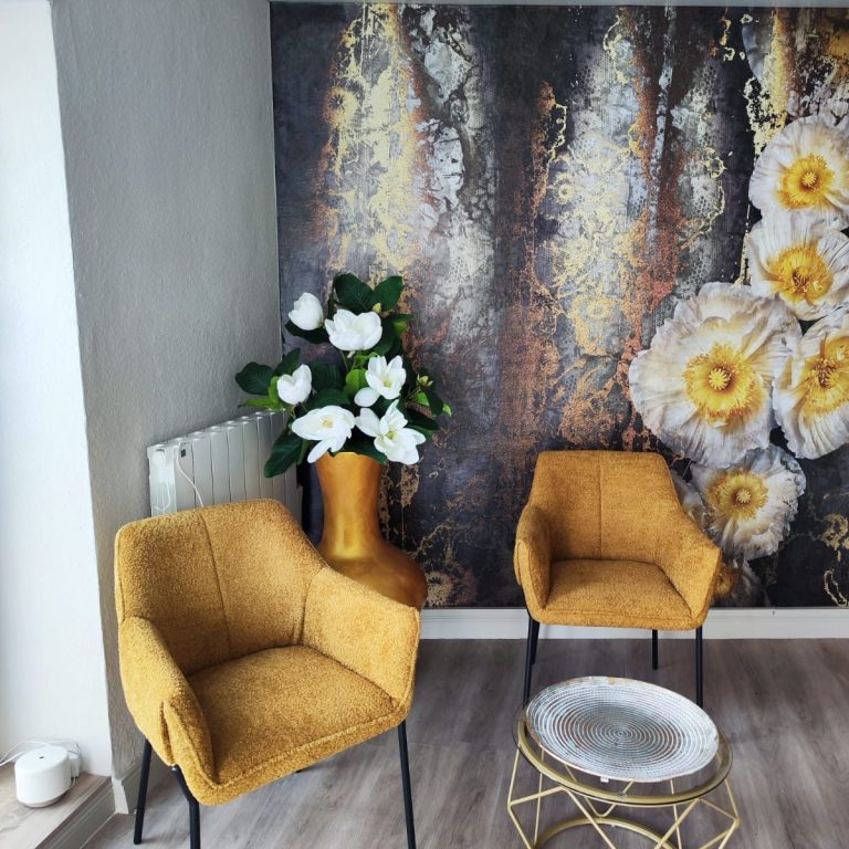 Wartebereich Zwei senfgelbe Stühle vor einer Wand mit Blumenmuster und einer Vase mit Blumen.